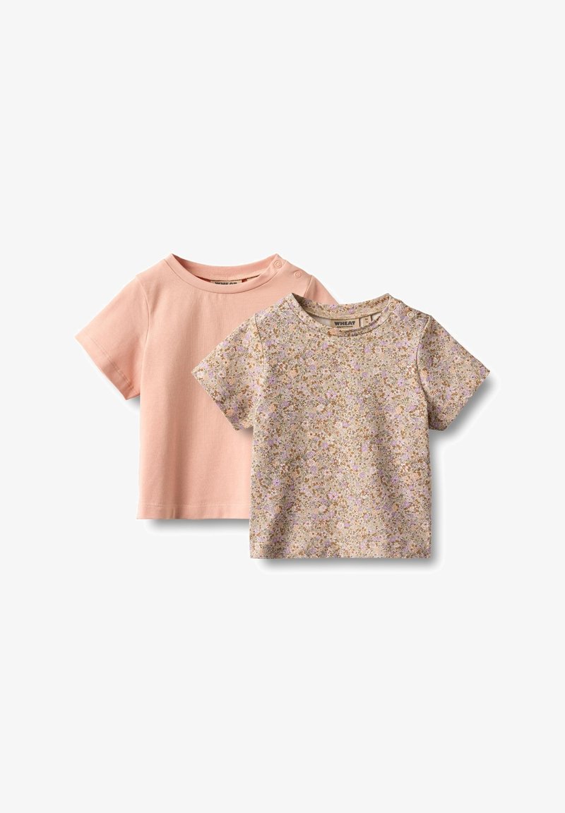 Dvě dětské trička s krátkým rukávem: jedno jednobarevné v světle růžové barvě, druhé s květinovým vzorem v pastelových barvách na béžovém pozadí.