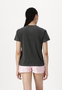 Camiseta de algodón gris oscuro con cuello redondo y mangas cortas, vista desde atrás, combinada con pantalones cortos rosas. Diseño simple, sin patrones.