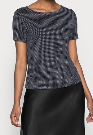 Granatowy top z krótkim rękawem w białe kropki, z okrągłym dekoltem, miękką teksturą materiału i luźnym krojem, zestawiony z czarną satynową spódnicą.
