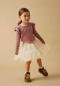 Jasnofioletowa bluzka z długim rękawem i falbanami na ramionach, połączona z warstwową białą spódnicą z tiulu i brązowymi botkami na sznurówki.