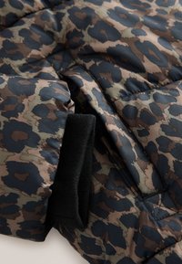 Gros plan d'une manche de veste matelassée avec un imprimé léopard marron, noir et gris et un poignet côtelé noir.