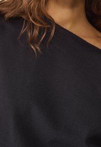 Czarny top z opuszczanymi ramionami wykonany z miękkiej tkaniny o gładkiej fakturze. Charakteryzuje się luźnym krojem i minimalistycznym designem.