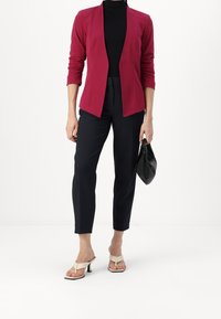 Burgundský blazer s uvolněným střihem a otevřeným předním dílem, zkombinovaný s černými úzkými kalhotami a béžovými sandály na podpatku. Černá psaníčko v ruce.