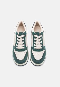 Sneakerid, millel on rohelisest sametist ja valgest nahast pealis, beežid paelad, polsterdatud keel ja kontrastne tume tald.