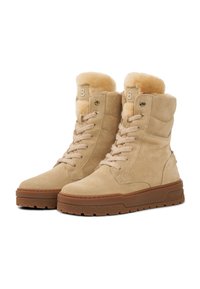 Béžové semišové kotníkové boty s měkkou kožíškovou podšívkou, kulatými tkaničkami a gumovou podešví. Mají kovové průchodky a vyražené logo na boku.
