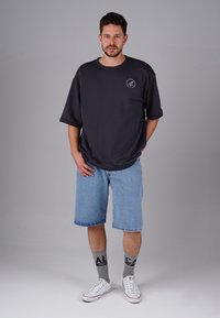 Dark grey oversized t-shirt with a round neckline, paired with light blue denim shorts. Grey socks with black lettering and white sneakers.