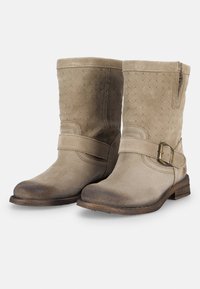 Botas de tobillo de ante beige con una correa de hebilla metálica, parte superior texturizada y puntera desgastada, que cuentan con un taco bajo y una cremallera lateral.