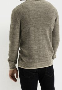 Maglione lavorato a maglia di colore grigio chiaro con un motivo testurizzato, scollo rotondo e maniche lunghe, abbinato a jeans in denim scuro.