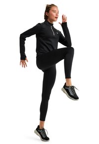 Zwart sportief langmouwen top met ritssluiting, aansluitende zwarte leggings en zwarte sneakers met mesh accenten, tegen een witte achtergrond.