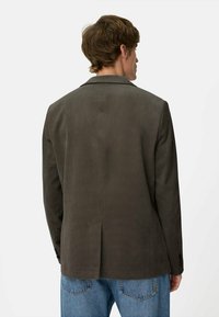 Mørkegrøn blazer lavet af struktureret stof, med reverskrave, enkelt splitventil bagpå og knapdetaljer på ærmerne.