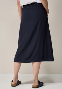 Gonna midi blu navy con elastico in vita, realizzata in un tessuto leggero e morbido, con tasche laterali. Abbinata a sandali e a un top semplice.