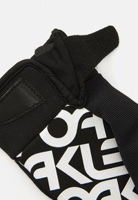 Les gants de sport noirs présentent un tissu texturé, une fermeture Velcro et un motif de logo blanc audacieux. Conçus pour offrir adhérence et soutien lors des activités.