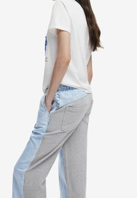 T-shirt blanc en coton associé à un pantalon patchwork gris et bleu clair. Le pantalon comporte des poches et une ceinture rayée.