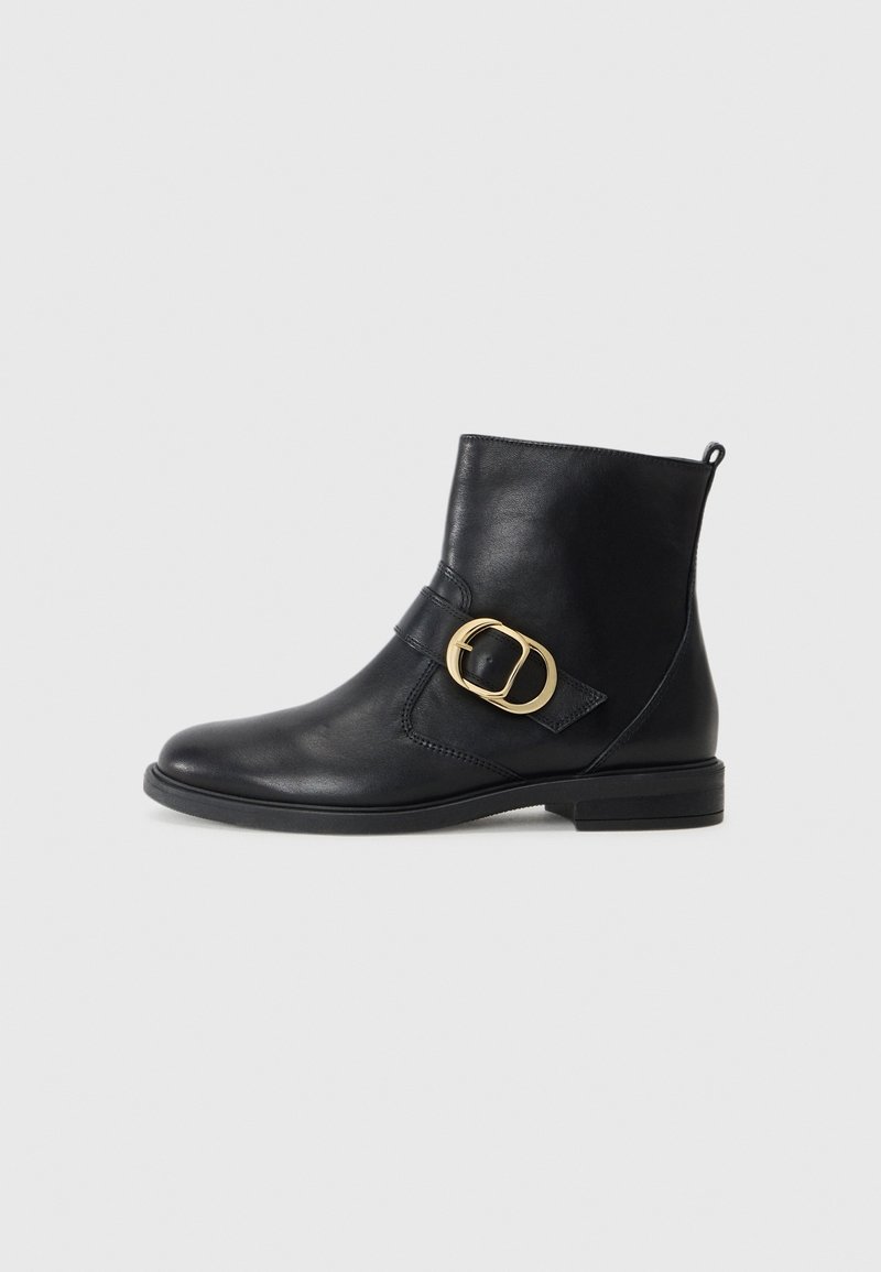 Bottine en cuir noir avec talon bas et grand détail de boucle dorée sur le côté, sur fond blanc.