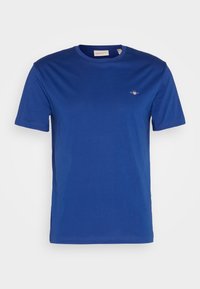 T-shirt en coton bleu à manches courtes avec col rond et petit logo blanc et rouge sur la poitrine gauche.