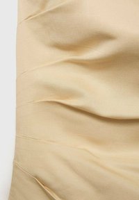 Tessuto beige con texture arricciata, caratterizzato da pieghe orizzontali e una superficie liscia. Il materiale appare leggero e leggermente lucido.