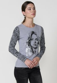 Camiseta de manga larga gris con un gráfico de cara en blanco y negro, mangas negras con estampado y un escote redondo. Detalle de tejido texturizado.