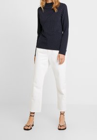 Mörkblå långärmad topp med vita prickar, med en omslagsdesign. Kombinerad med vita vida byxor och svarta sandaletter med remmar.