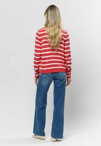 Červeno-krémová pruhovaná košeľa s dlhým rukávom a voľným strihom, kombinovaná s vysokým pásom modrých rozšírených džínsov. Textúrované pleteniny a denimové materiály.