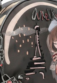 Zaino rotondo in pelle scura con ricamo della Torre Eiffel rosa, dettagli metallici e un charm decorativo a forma di gatto. Presenta una superficie liscia e diverse texture.