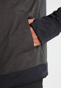 Grå texturerad tygtröja med en mörkblå nederkant och ärmmanchetter. Har en sidoficka för bekvämlighet.