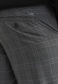 Graue karierte Hose aus strukturiertem Stoff mit einem Knopfverschluss und einem kleinen Markenetikett auf der Rückentasche.
