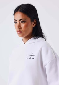 Witte hoodie van zacht materiaal, met een voorzak in kangoeroestijl en een klein zwart logo op de borst. Bevat een capuchon met trekkoord.