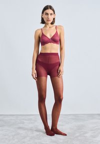 Bralet de dantelă maroon cu bretele ajustabile, asortat cu pantaloni scurți maroon din tul cu talie înaltă și ciorapi maroon cu buline. Textură netedă.