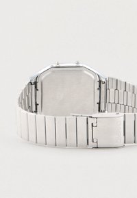 Ασημένιο μεταλλικό ρολόι με οκτάγωνη κάσα και μπρασελέ από ανοξείδωτο ατσάλι. Διαθέτει γυαλιστερό φινίρισμα και κούμπωμα με την ένδειξη "CASIO".