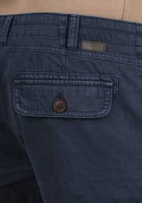 Marineblaue Baumwollshorts mit einer Gesäßtasche, die mit einem Knopfverschluss und einem Markenlabel ausgestattet ist. Sie weisen subtile Textur- und Nähdetails auf.