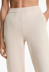 Light beige knitted pants with a ribbed elastic waistband, featuring side pockets and a relaxed fit, showcasing a soft texture.