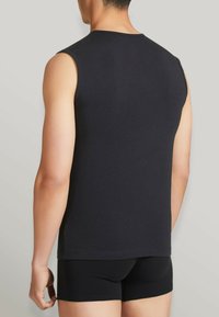 Maglietta nera senza maniche in cotone, con scollo rotondo e design semplice. Abbinata a pantaloni corti neri visibili sul fondo.