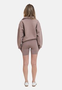 Světle hnědá oversized mikina s kleslými rameny, v kombinaci s odpovídajícími přiléhavými cyklistickými šortkami. Má hladkou tkaninu a minimalistický design.