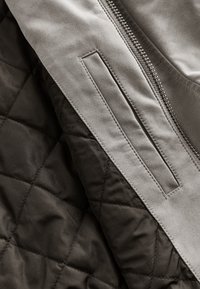 Gros plan d'un tissu noir matelassé avec une section en cuir gris lisse adjacente présentant une poche rectangulaire cousue et un détail de fermeture éclair.