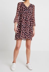 Häikäisevä, polvipituinen mekko tummansinisellä pohjalla, jossa on sydämen muotoja punaisena ja valkoisena. Mekossa on syvä V-kaula-aukko ja läpinäkyvät kolmenneljänneksen hihat.