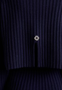 Tissu en maille côtelée bleu marine foncé avec un petit bouton décoratif en métal en forme de fleur au-dessus d'une fente verticale.
