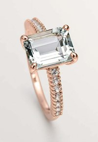Gema transparente de corte cuadrado engastada en una banda de oro rosa con pequeñas piedras blancas de acento a lo largo de la caña y textura retorcida.