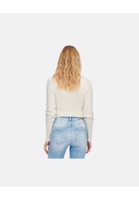 Pull en tricot blanc à manches longues et coupe courte, associé à un jean taille haute bleu clair. Texture lisse, style décontracté.
