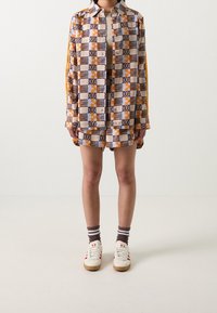 Knapp-up skjorta med ett geometriskt mönster i orange, blått och krämfärgat; bärs med matchande shorts, vita sneakers och randiga strumpor.