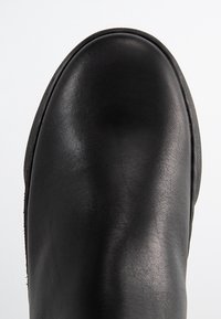 Bottine en cuir noir à texture lisse, bout arrondi et détails couturés. Fermeture éclair latérale pour faciliter l'enfilage.