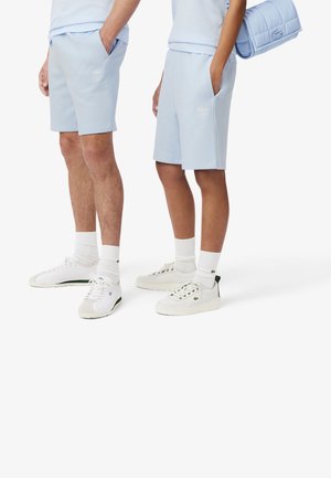 Light blue shorts, cotton blend, featuring side pockets. White sneakers with subtle branding and textured soles complement the look.