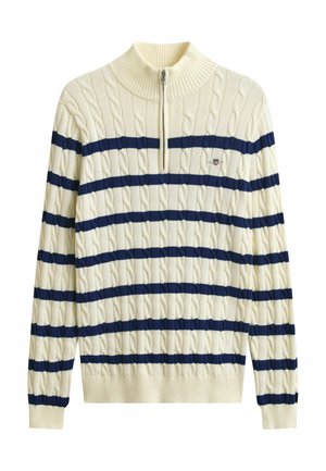 Krémový svetr s copánkovým vzorem, námořnicky modrými vodorovnými pruhy, půlzipsovým límcem, dlouhými rukávy a malým vyšívaným znakem na hrudi.