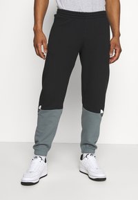 Svarta och grå mjukisbyxor med elastisk midjeband, med en avsmalnande design och kontrasterande ljusgrå nedre paneler.