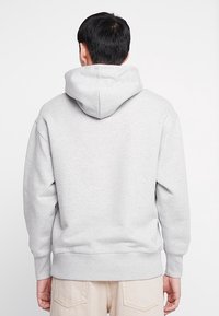 Felpa grigia con tasca a marsupio, polsini e orlo a costine. Presenta un grande cappuccio con una texture semplice e morbida e una vestibilità rilassata.