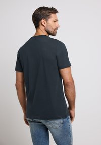 Tmavě šedé tričko s krátkým rukávem vyrobené z měkkého materiálu, s klasickým kulatým výstřihem a volnějším střihem, v kombinaci s modrými džíny.