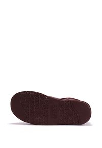 Suela de zapato burdeos con un patrón de agarre texturizado y una marca en relieve. El material parece duradero, con un diseño plano y bordes redondeados.