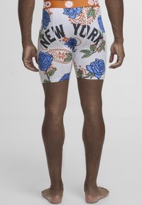 Boxershorts med hvit bunn, blå rosemønster og oransje detaljer, med teksten "NEW YORK" i fet svart skrift på baksiden.