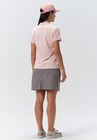 Vaaleanpunainen polo-paita, harmaat shortsihameet ja harmaat sandaalit. Polossa on kaulus ja lyhyet hihat. Shortsihameessa on takavetoketju joustavuutta varten.