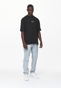 T-shirt nera a maniche corte con testo bianco, abbinata a jeans in denim azzurro chiaro e sneakers bianche. Design semplice e dalla vestibilità rilassata.