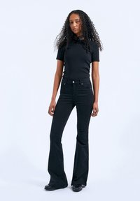 Black flared jeans with a fitted black t-shirt. Smooth texture, standard five-pocket design, and subtle metal hardware details.